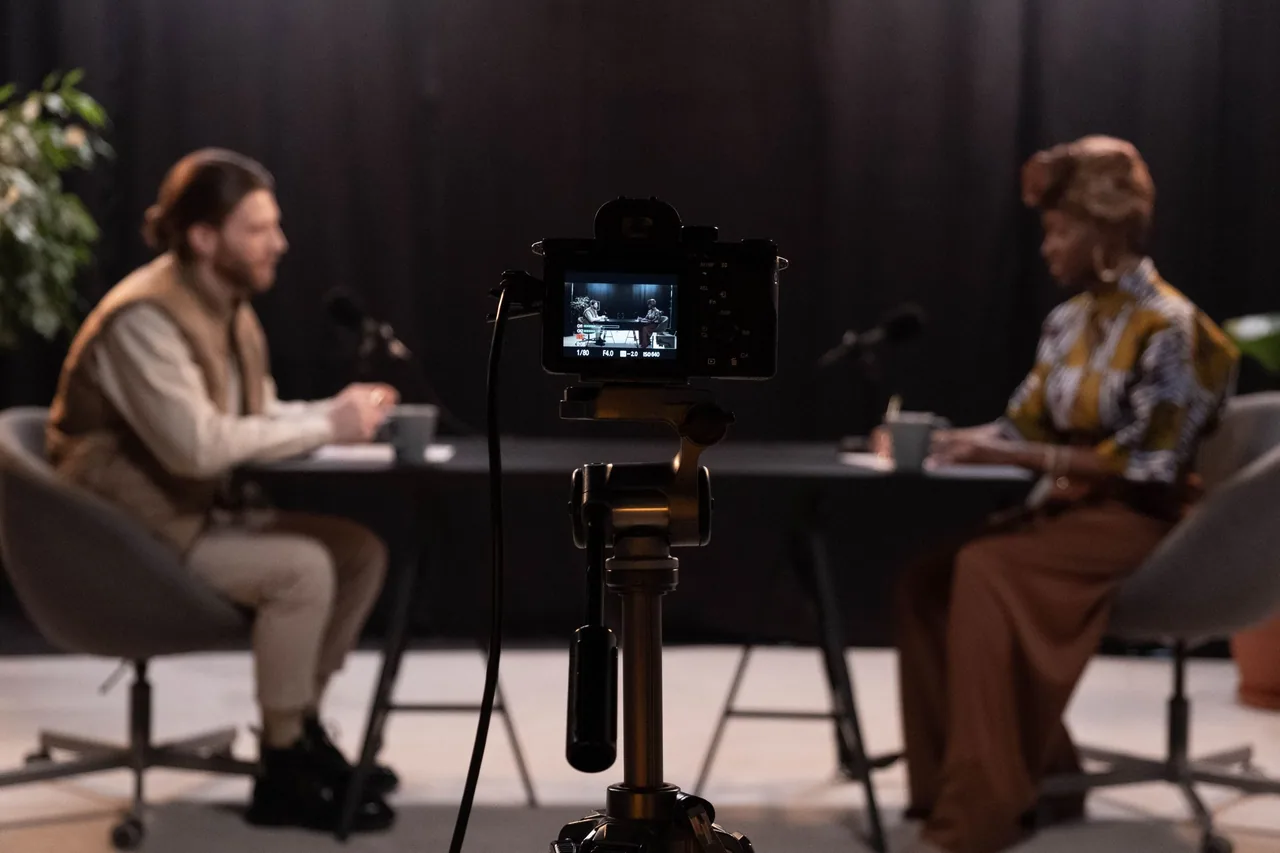 A camera records a podcast conversation in a studio